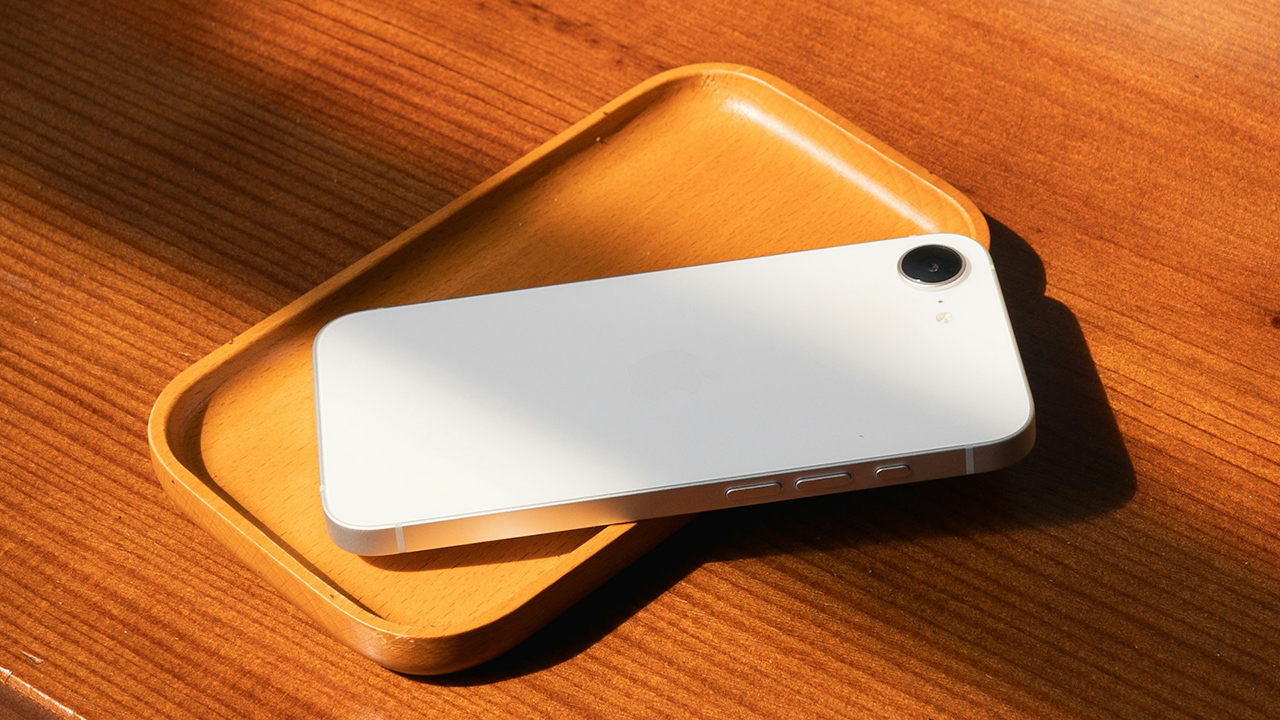 Foto do iPhone 16e na cor branca em cima de um prato retangular de bambu