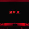 Uma televisão com a tela preta exibindo o logo da Netflix; a TV emite uma luz vermelha na parede atrás dela