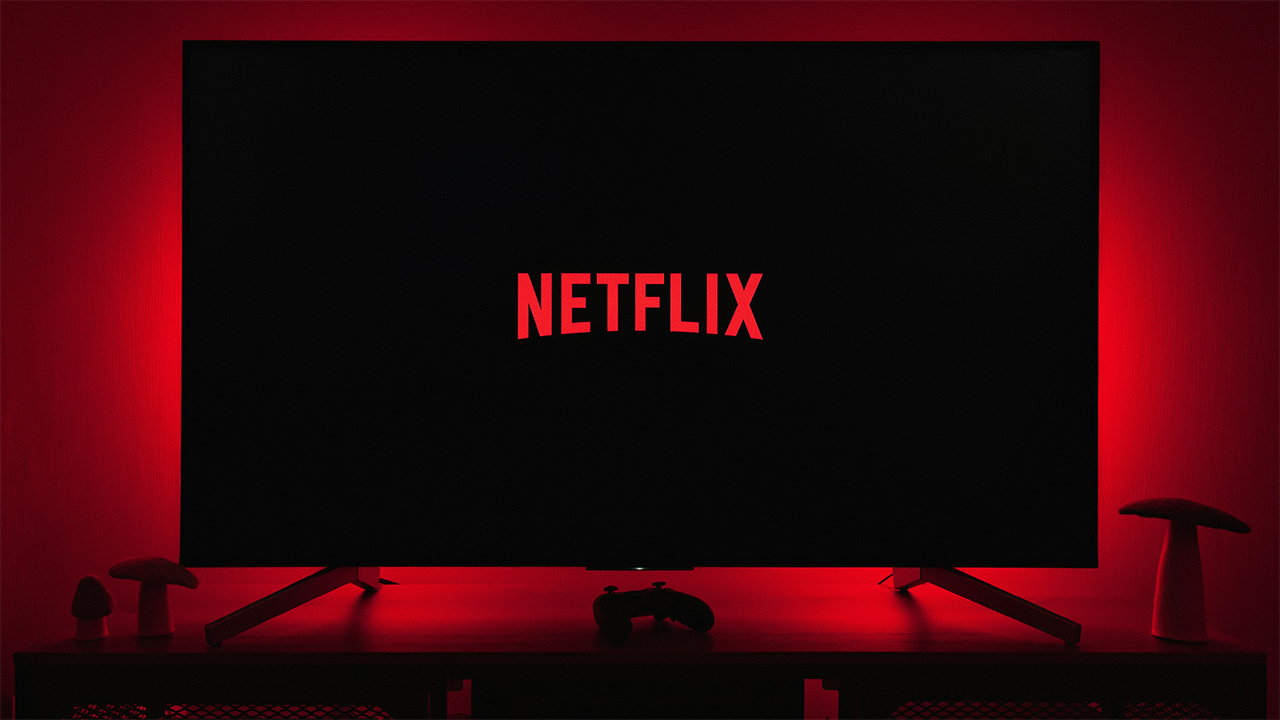 Uma televisão com a tela preta exibindo o logo da Netflix; a TV emite uma luz vermelha na parede atrás dela
