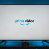Uma televisão com a tela branca exibindo o logo do Prime Video; a TV emite uma luz azulada na parede atrás dela