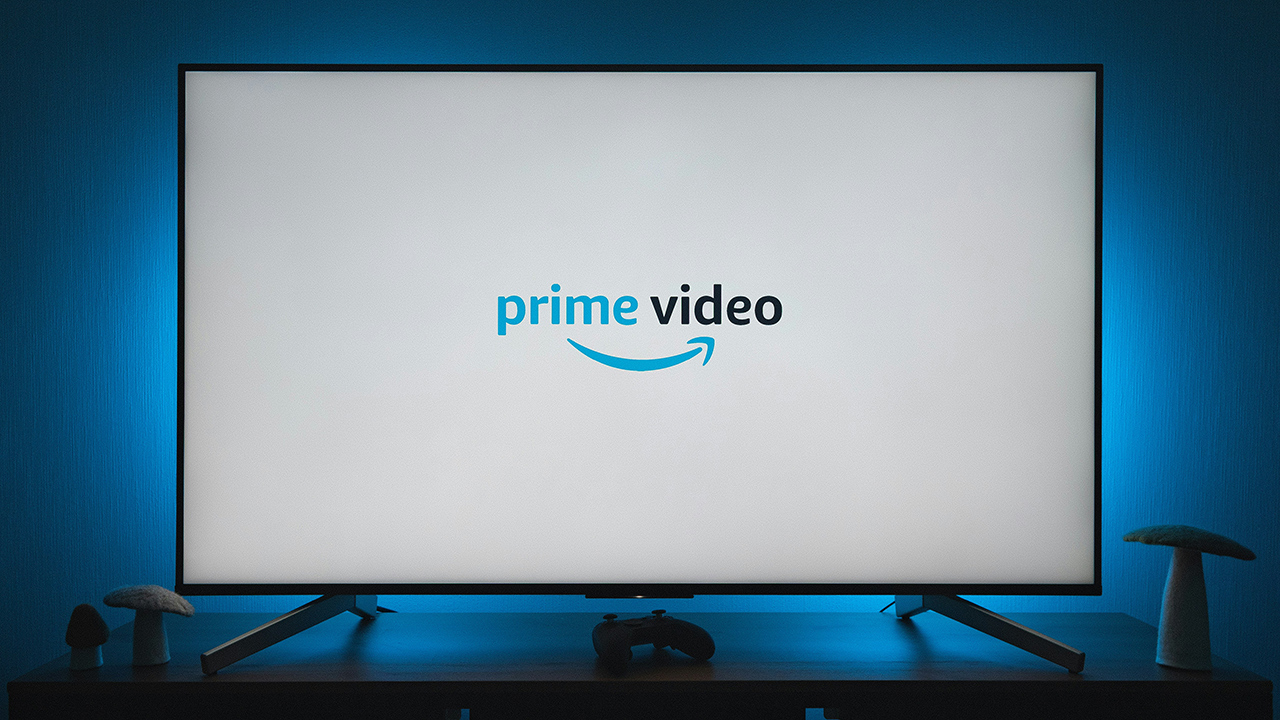 Uma televisão com a tela branca exibindo o logo do Prime Video; a TV emite uma luz azulada na parede atrás dela