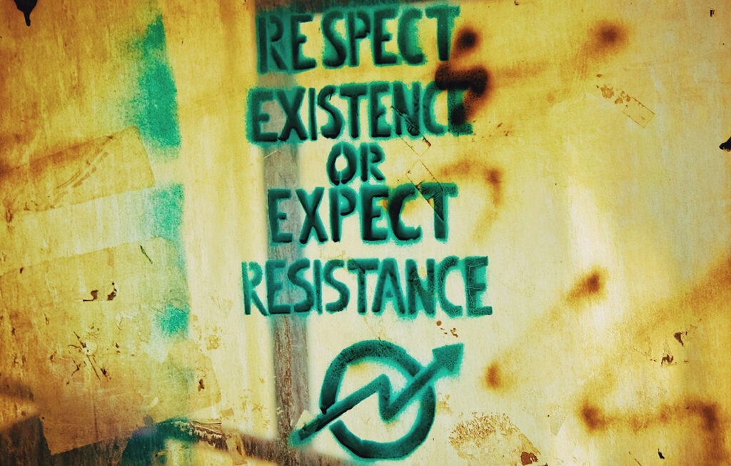 Foto de um muro com a frase pixada "respect existence or expect resistance" (respeite a existência ou encare resistência)