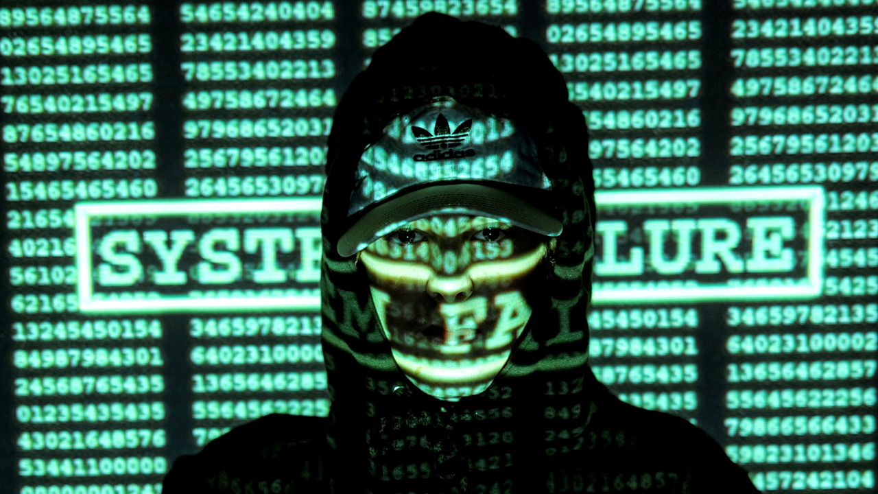 Uma pessoa com capuz e boné tem o rosto encoberto por sequências escritas em verde e a expressão "system failure"