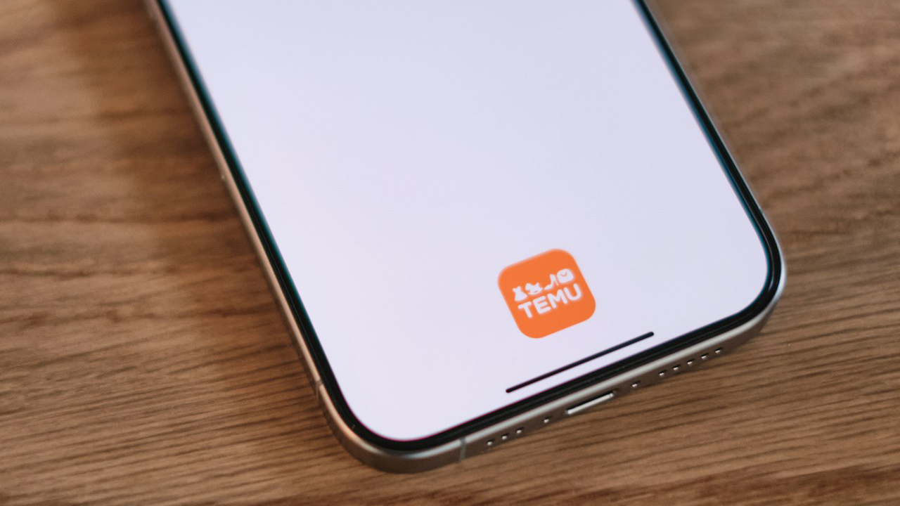 Foto de um celular com a tela em branco e o ícone do app Temu, em laranja, no canto inferior