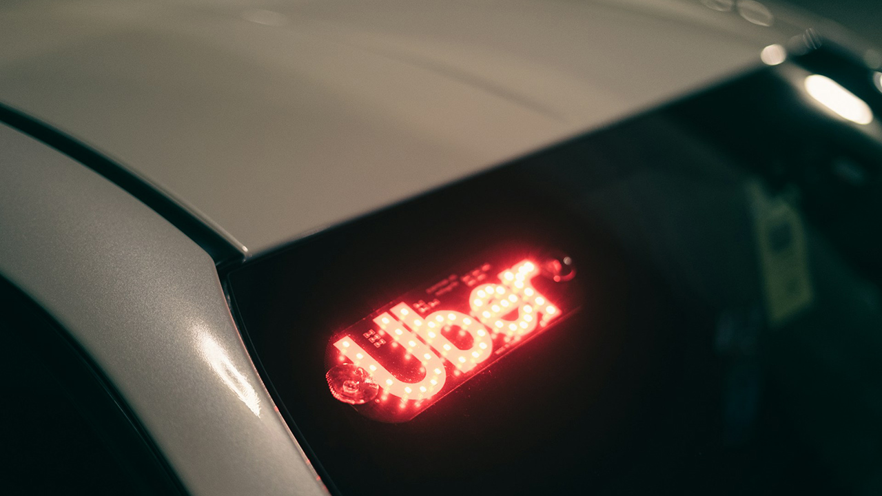 Foto do para-brisa de um carro com o letreito luminoso escrito Uber