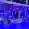 Logo da Jovi em neon na entrada de um estabelecimento. As letras estão na cor azul