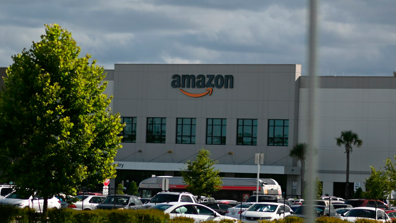 Foto de um prédio da Amazon em meio a uma árvore e um poste, com o estacionamento em frente