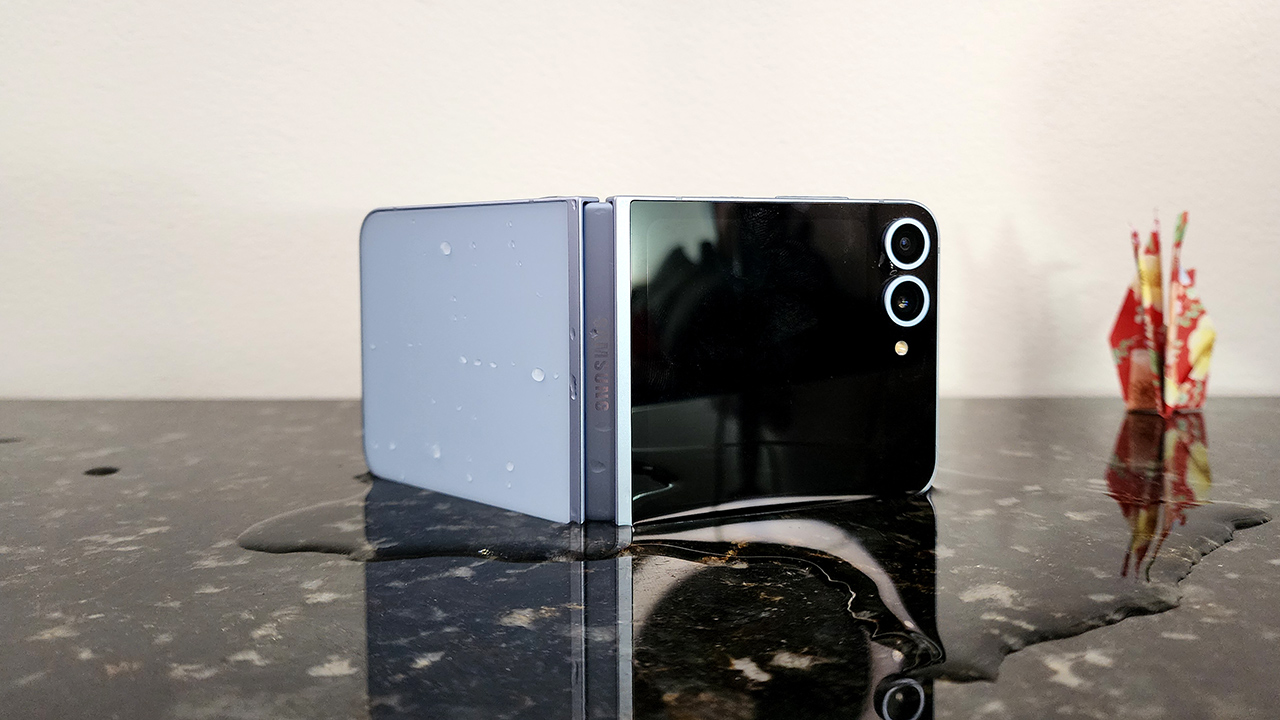 Foto do Galaxy Z Flip 6 ligeiramente aberto e de lado em uma mesa com água