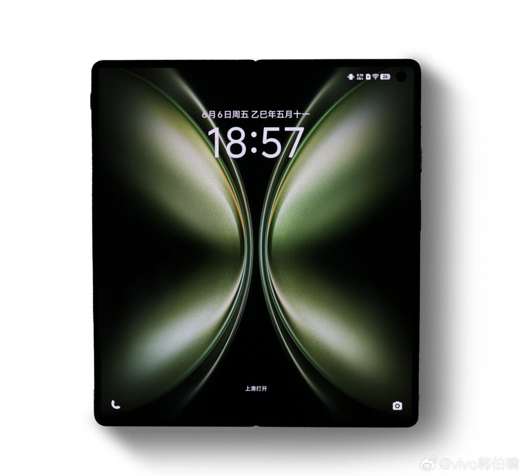 Uma imagem da parte frontal do Vivo X Fold 5 aberto, com um papel de parece que parece uma borboleta verde com as asas abertas. Tem alguns textos em chinês, além de informações comuns como data, horário, rede e bateria (26%)
