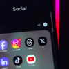 Foto de um celular na pasta 'Social' com os ícones de Facebook, Instagram, Threads, X/Twitter, LinkedIn, TikTok e YouTube
