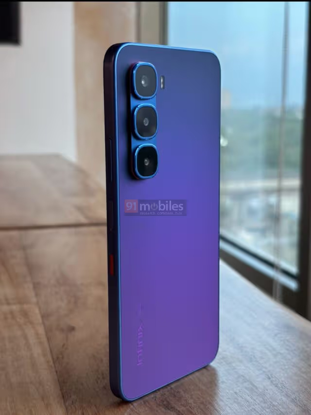 Um celular na cor azul em pé sobre uma bancada de madeira. Ele tem um módulo de câmeras com três sensores alinhados na vertical