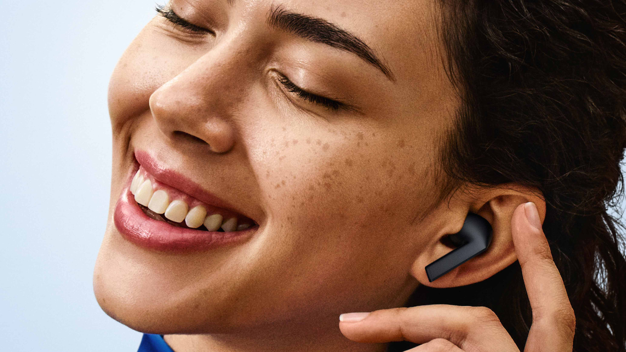 Uma mulher está com o Galaxy Buds 3 FE no ouvido. Ela sorri e prepara para tocar o dispositivo