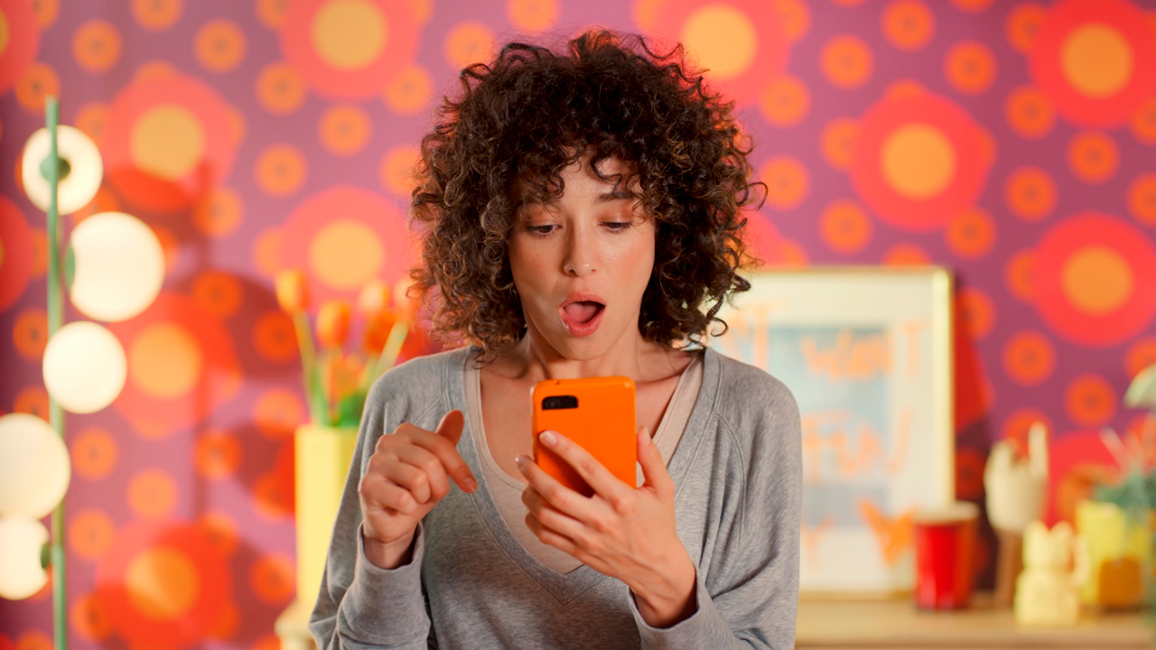 Uma mulher faz compras em um celular com cpaa laranja; quase todos os elementos da imagem têm tonalidades de laranja