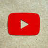 Ícone do YouTube feito em papelão vermelho recortado e colocado sobre um papelão sem tintura