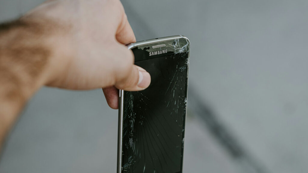 Uma pessoa segura um celular Samsung com a tela quebrada como se estivesse prestes a jogar no lixo