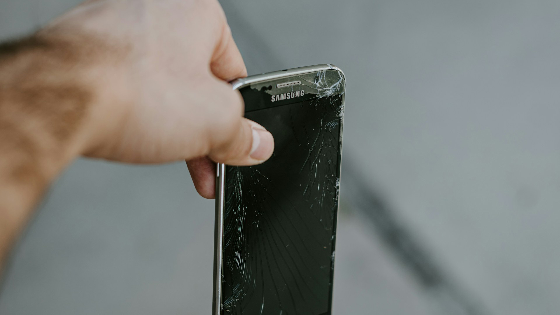 Uma pessoa segura um celular Samsung com a tela quebrada como se estivesse prestes a jogar no lixo