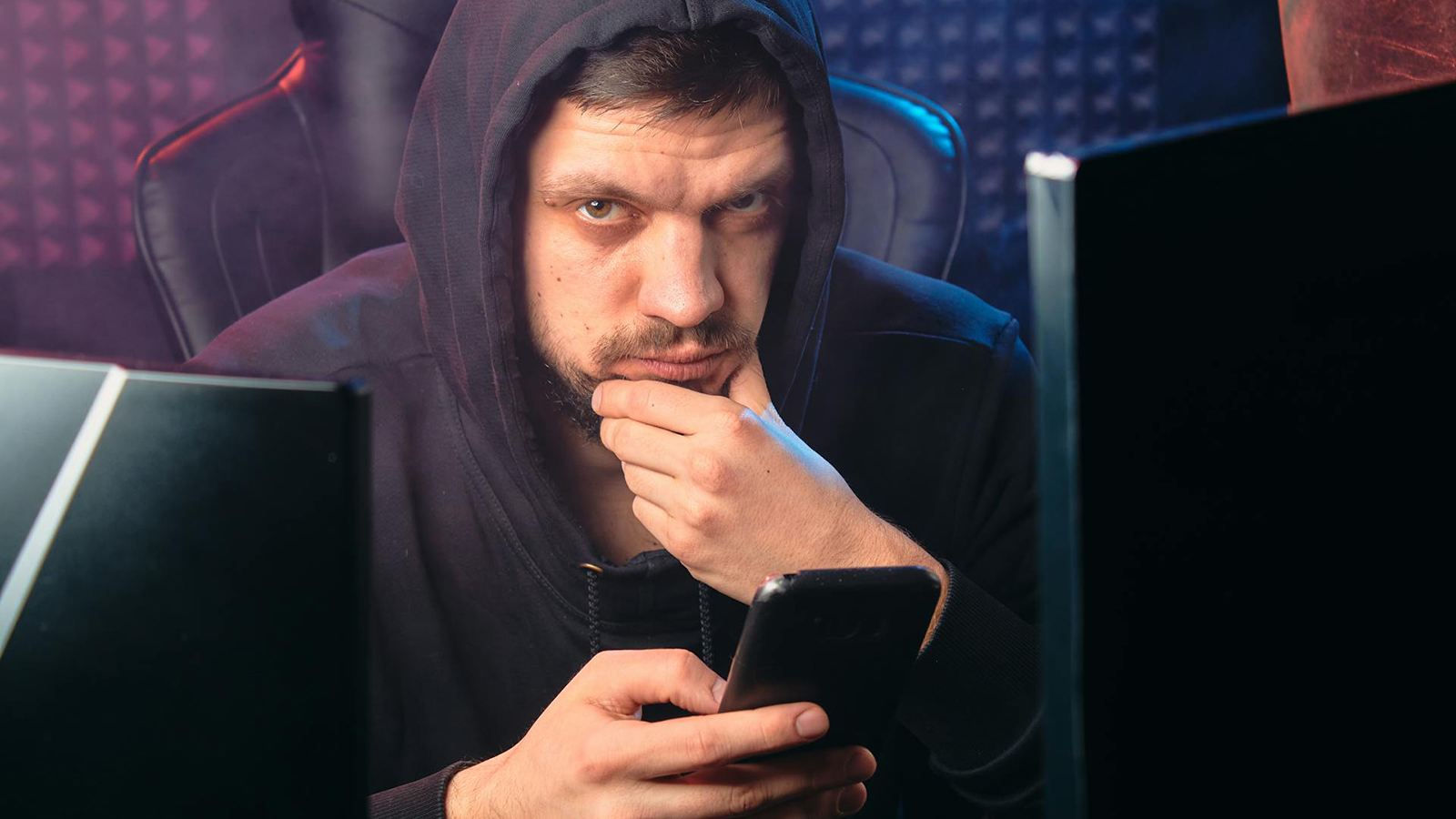 Privacidade em risco (um homem olha com cara pensativa para a câmera enquanto navega no celular; ele usa um moletom e o capuz ocbre sua cabeça)