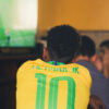 Uma pessoa com a camisa do Brasil com nome Neymar Jr assiste a um jogo de futebol na TV