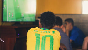 Uma pessoa com a camisa do Brasil com nome Neymar Jr assiste a um jogo de futebol na TV