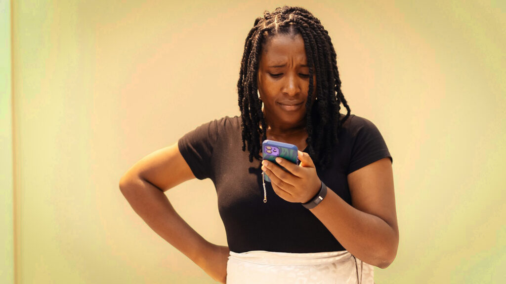 Uma mulher olha para o celular com expressão séria com a mão na cintura