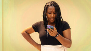 Uma mulher olha para o celular com expressão séria com a mão na cintura