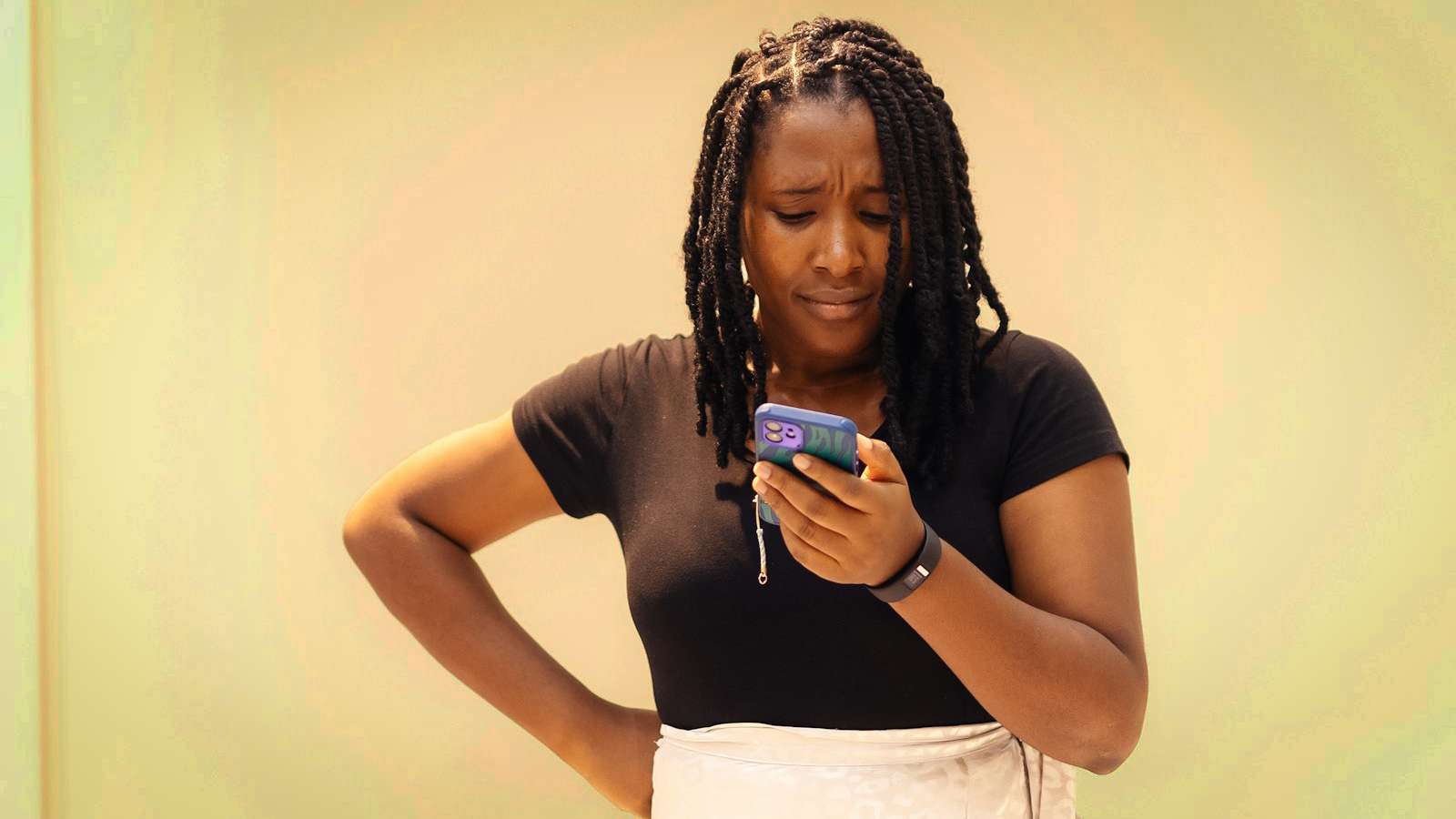 Uma mulher olha para o celular com expressão séria com a mão na cintura