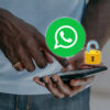 Uma pessoa segura um celular com o ícone do WhatsApp e um cadeado aberto acima da tela